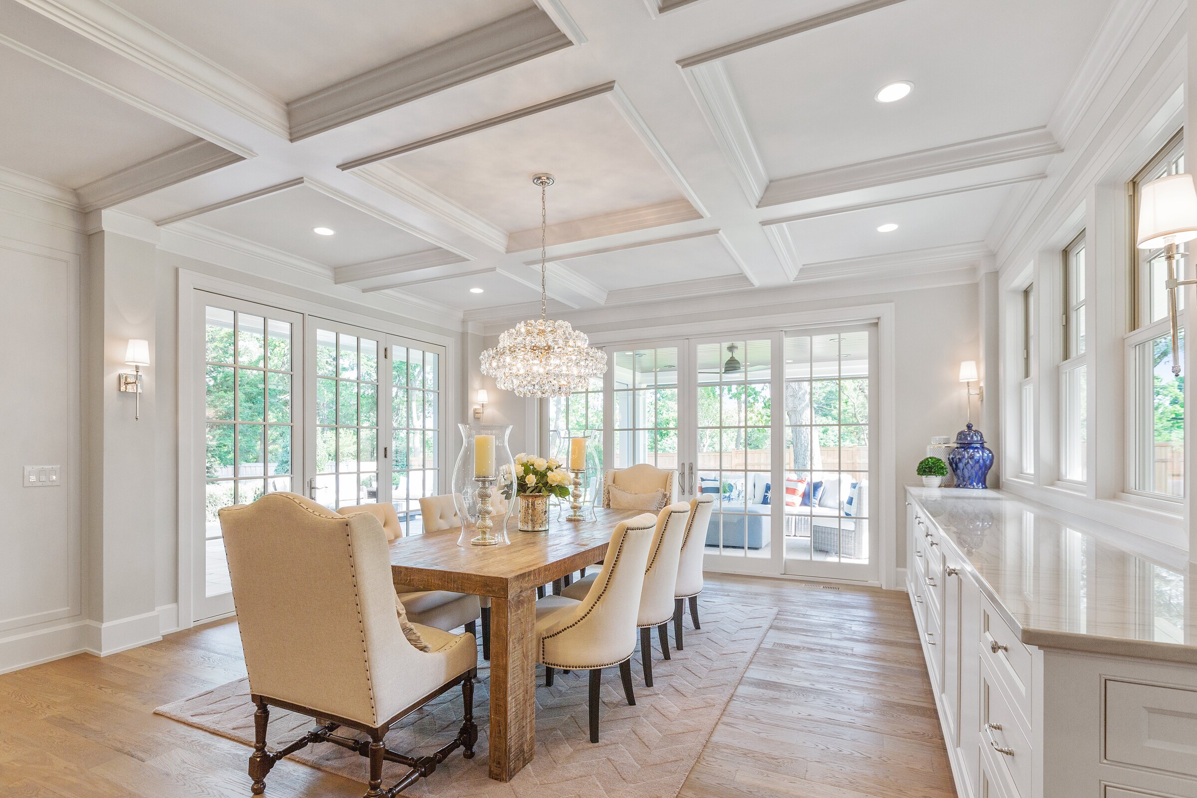 High-resolution real photograph of a bright dining room with white coffered ceiling, built-up crown moulding, and paneled walls