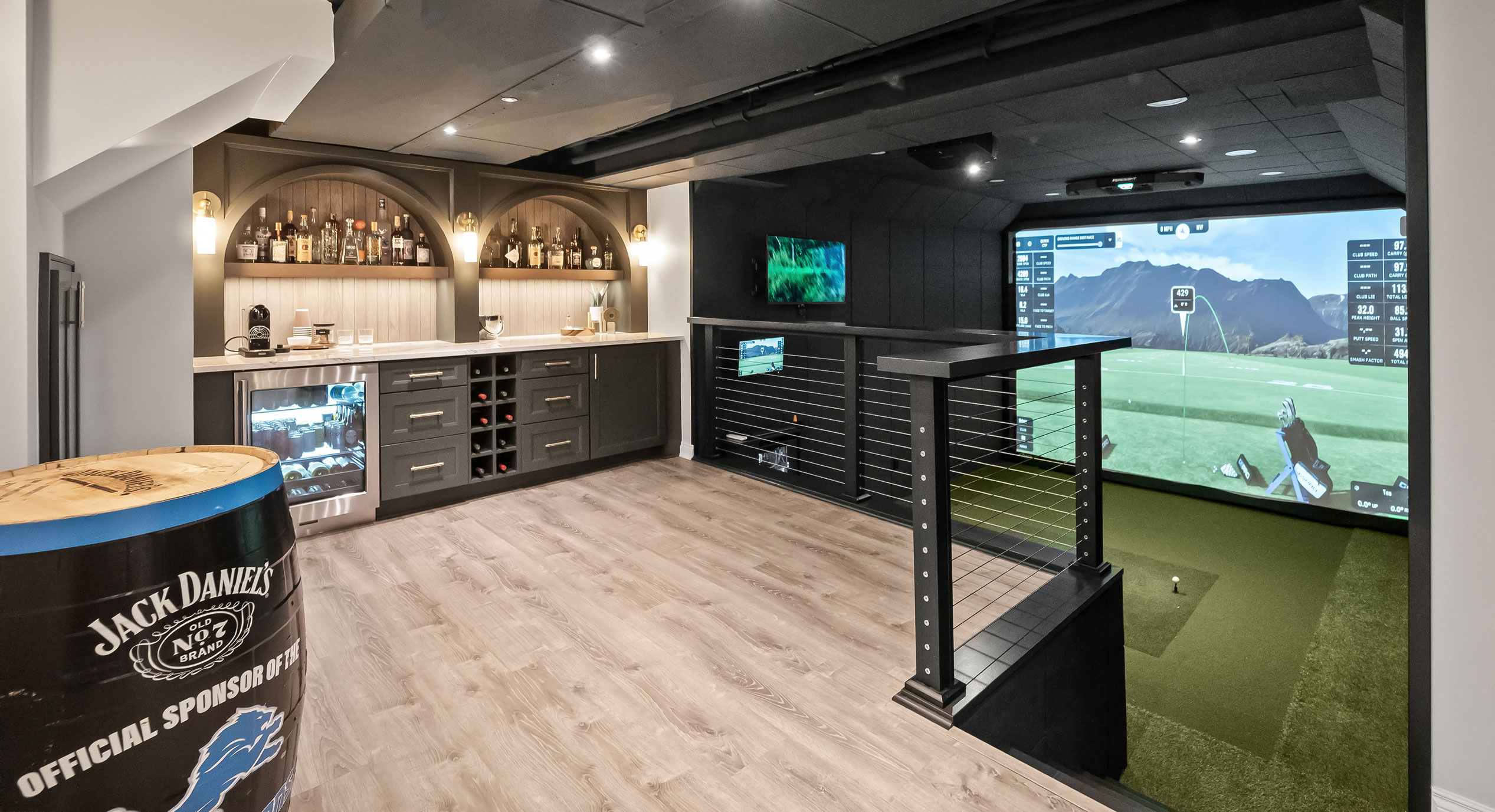 Finished basement with custom arched bar niches, fitted cabinetry, and a golf simulator lounge