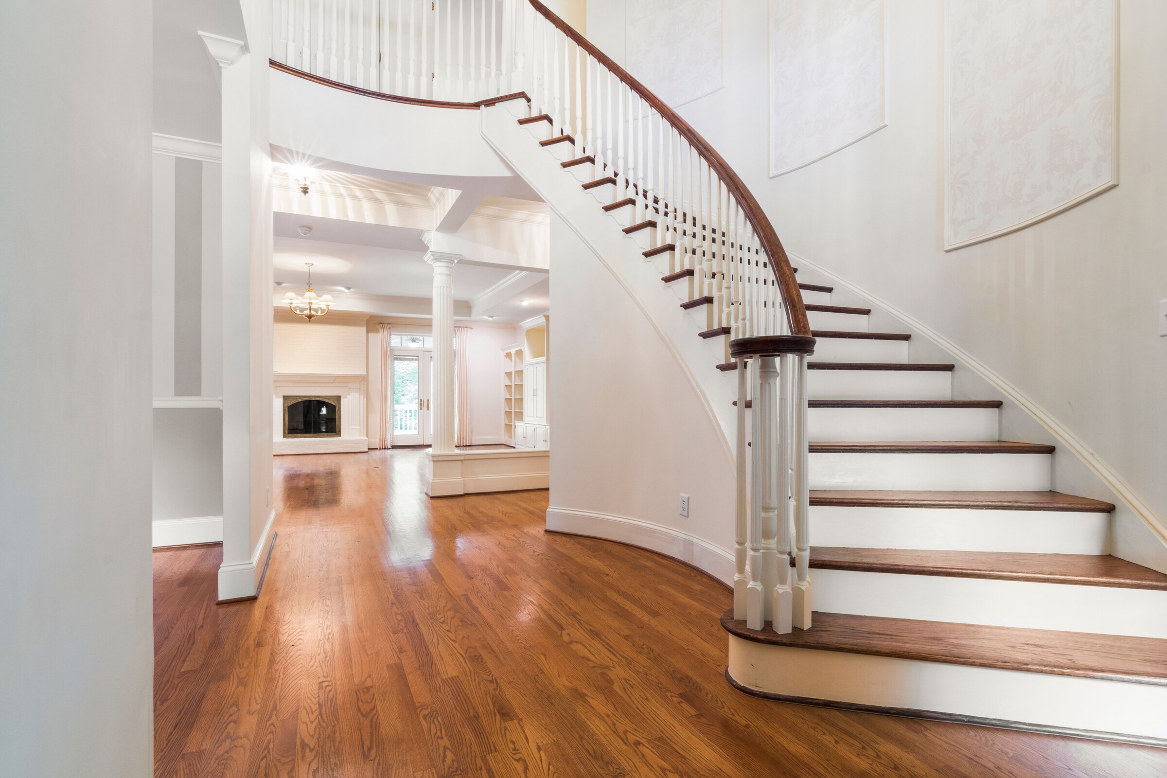 High-resolution real photograph of a grand curved staircase with stained oak treads and handrail, white risers, and white balusters